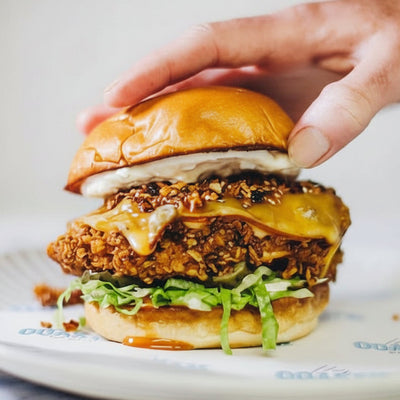 Hand holding a chicken sandwich on a plate with a blurred background